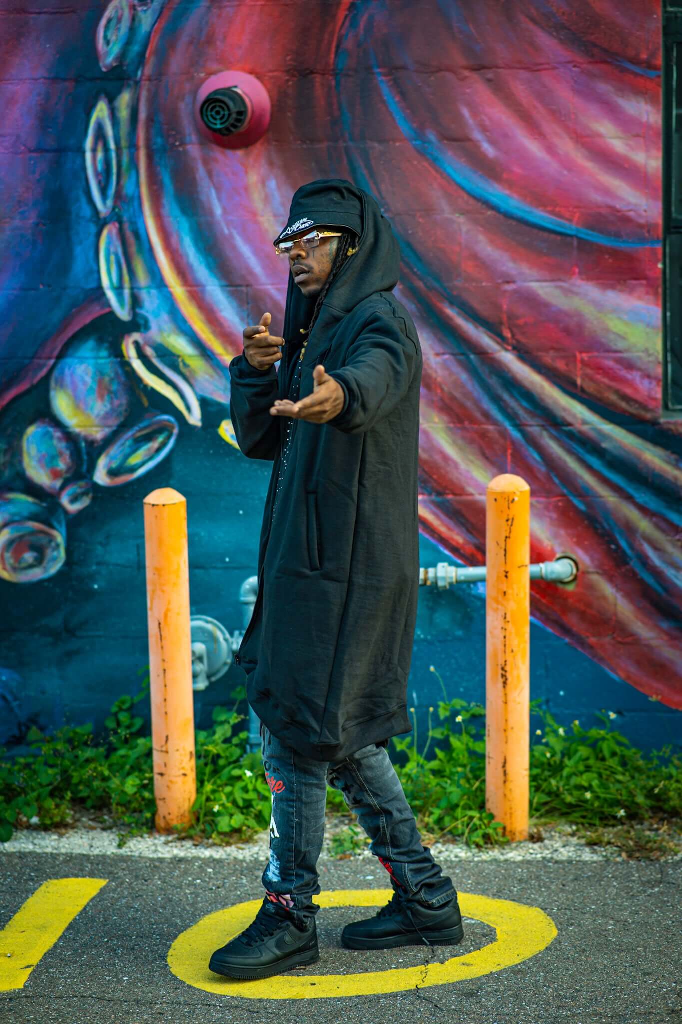 Marathon Hoodie | Avoir Fall Season worn by a model against a colorful mural, showcasing urban streetwear style.