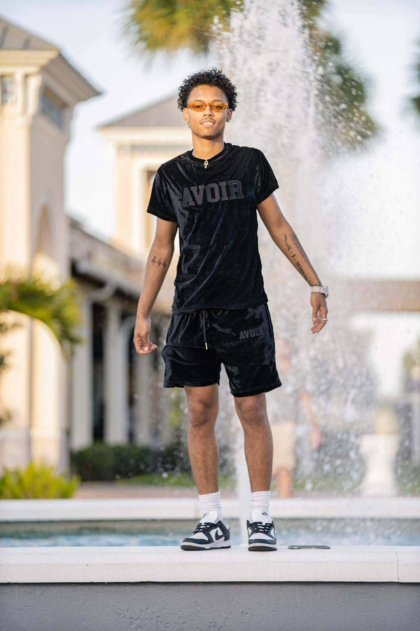 Man wearing black velour short set standing by fountain outdoors summer collection